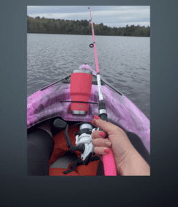A person holding a pink fishing rod in a kayak.