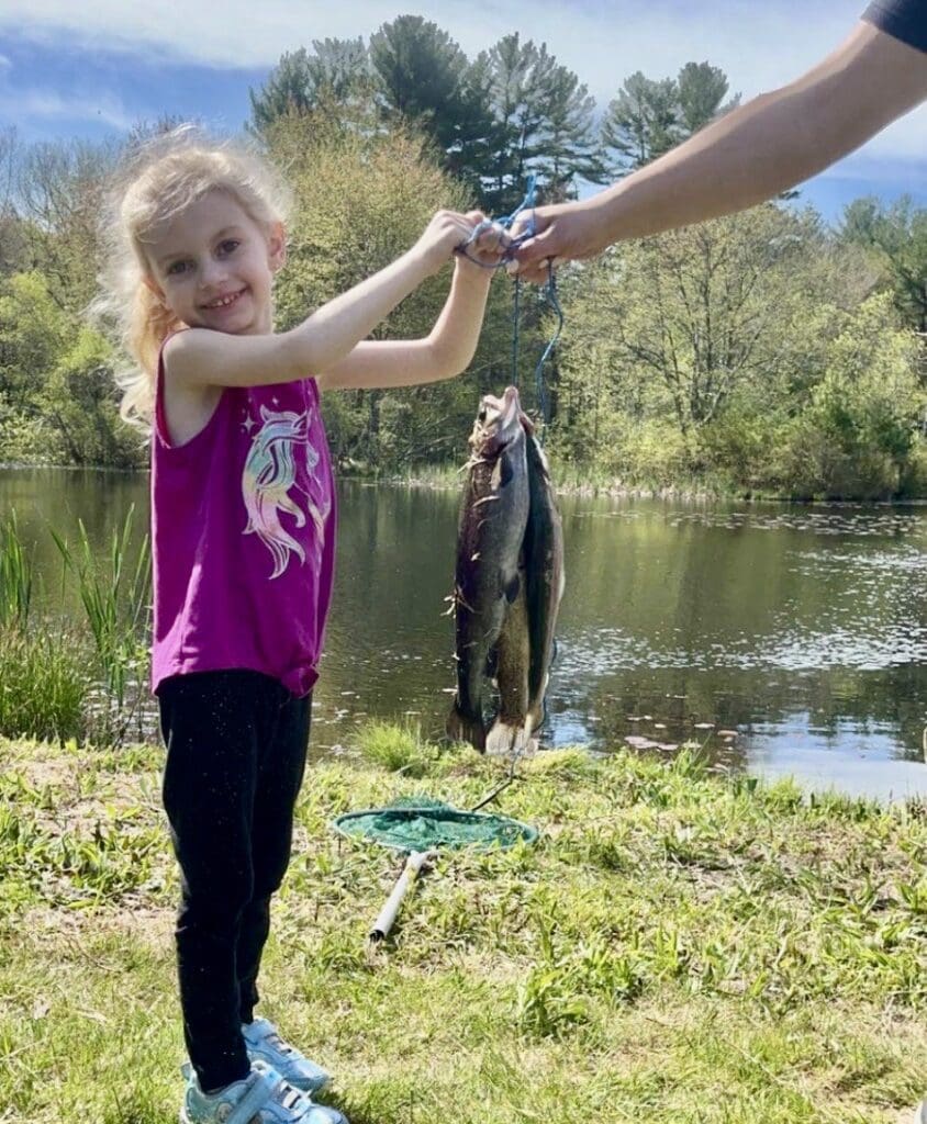 A little girl holds up a fish in front of a man.