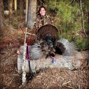 A woman holding a turkey in the woods.