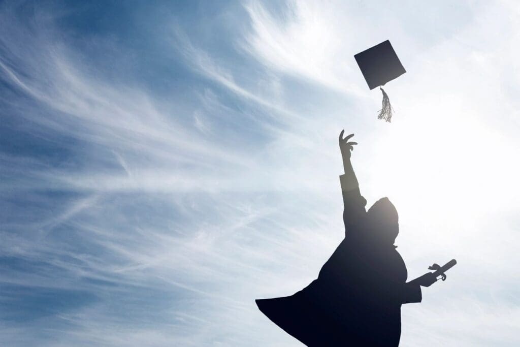 A silhouette of a person tossing a graduation cap in the air.