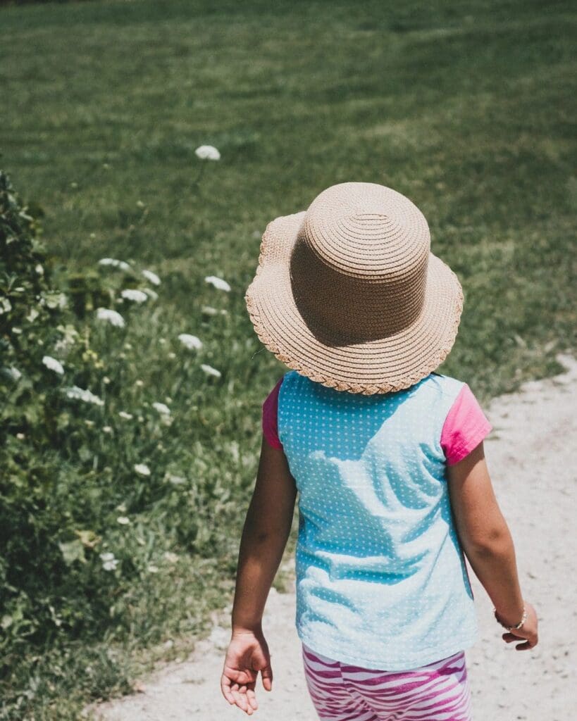 A little girl walking down a dirt path with a hat on.