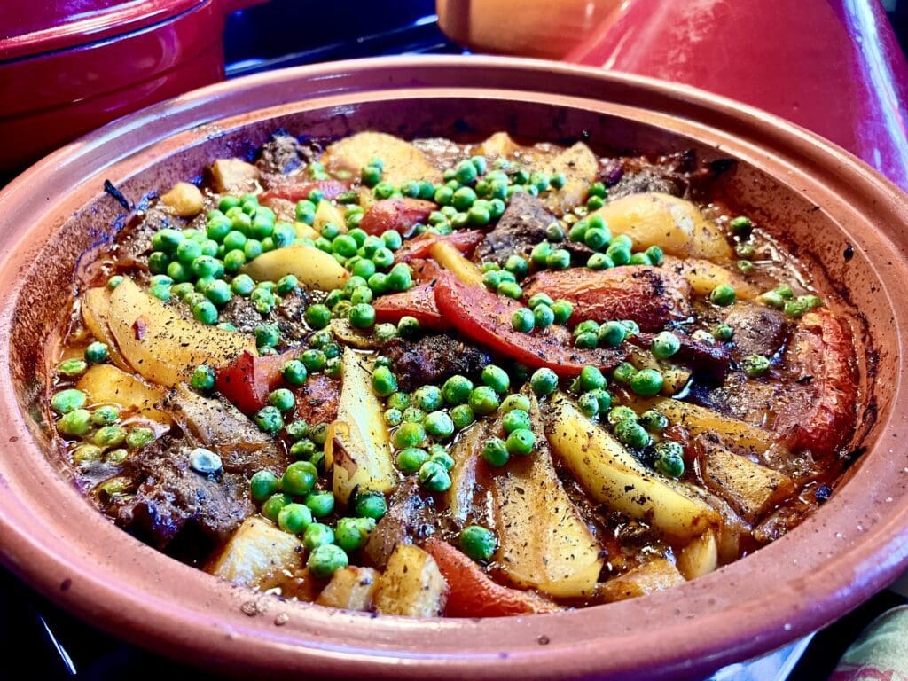 A clay pot with meat, vegetables, and peas.