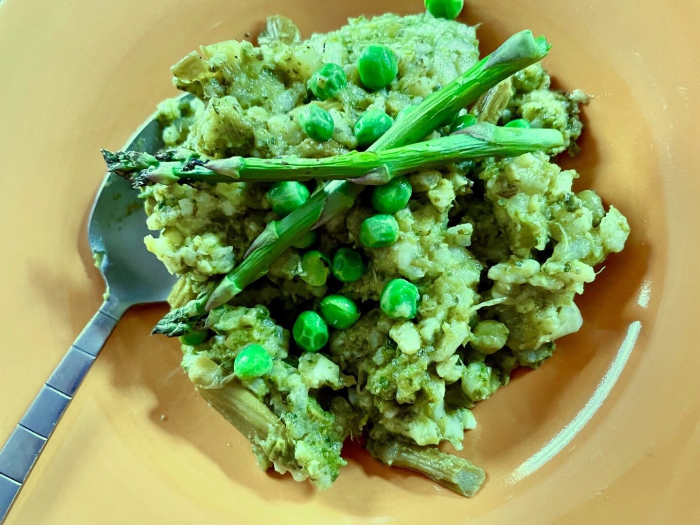 Risotto with asparagus and peas on an orange plate.