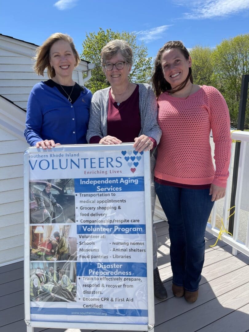 Three women standing in front of a sign that says volunteers.