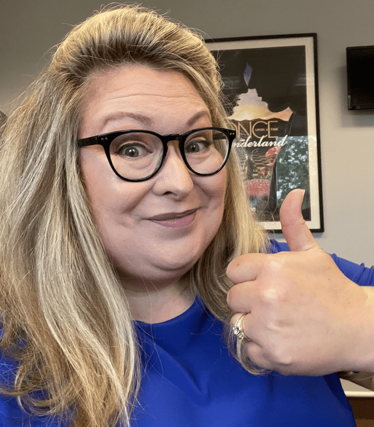 A woman in glasses giving a thumbs up.