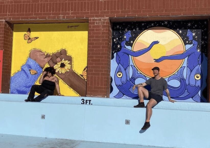 Two people sitting on a wall next to a mural.