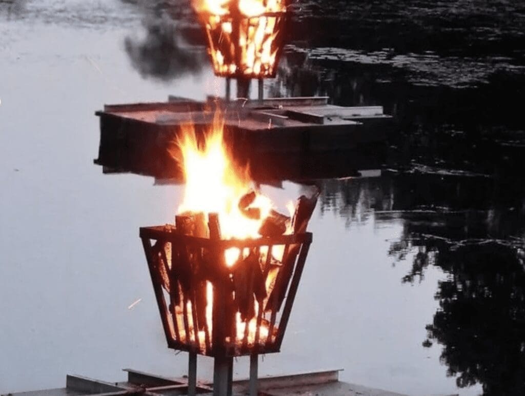 Two baskets with fire on top of a body of water.