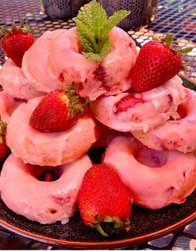 A plate of donuts topped with strawberries and mint.