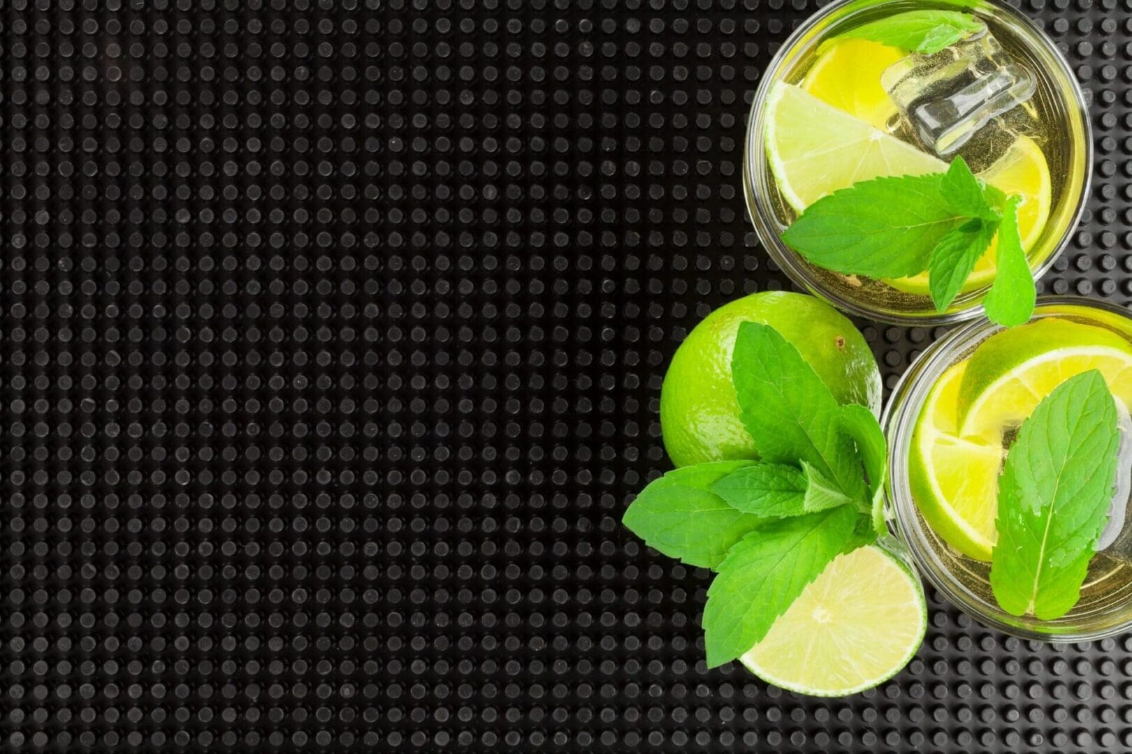 Two glasses of lemonade with mint leaves on a black background.