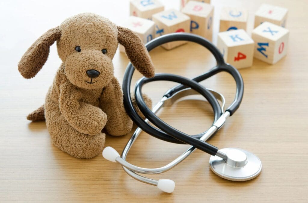 A teddy bear sits next to a stethoscope and blocks.