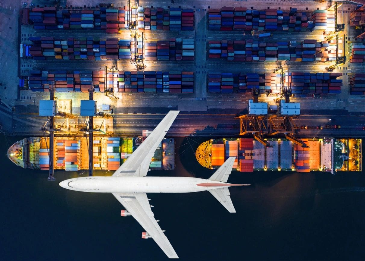 An airplane is flying over cargo containers at night.
