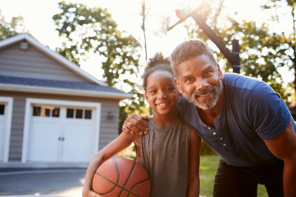 A man and a girl holding a basketball in front of a house.