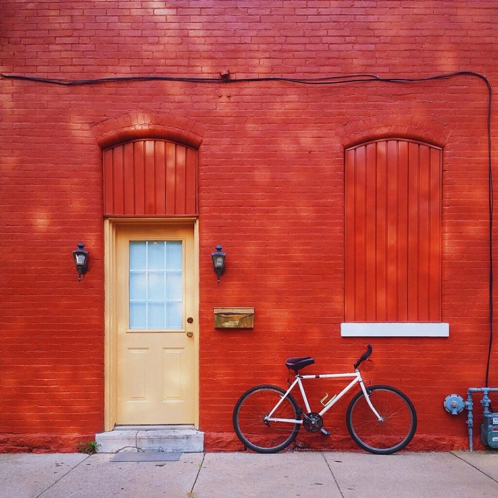 A bicycle is leaning against a red building with a yellow door.