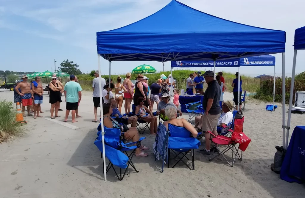 A group of people sitting under a blue tent on the beach.