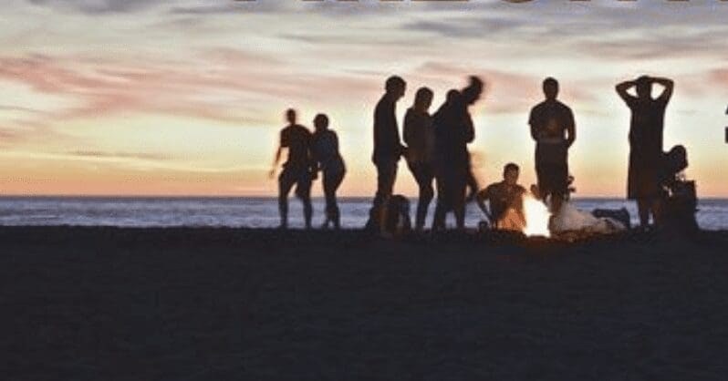 A group of people standing around a campfire at sunset.