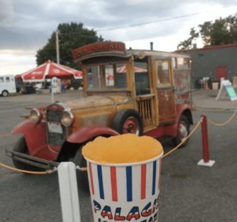 A vintage car with a bucket of popcorn in front of it.