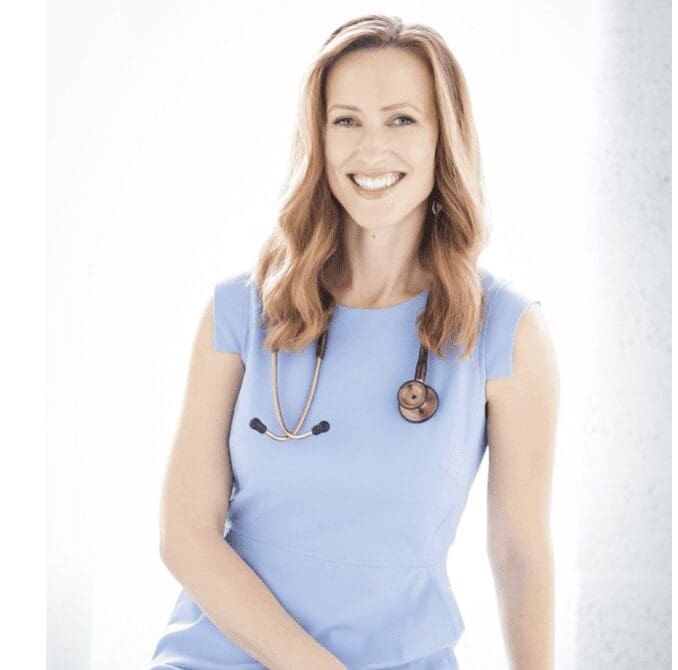A smiling woman in a blue dress with a stethoscope.