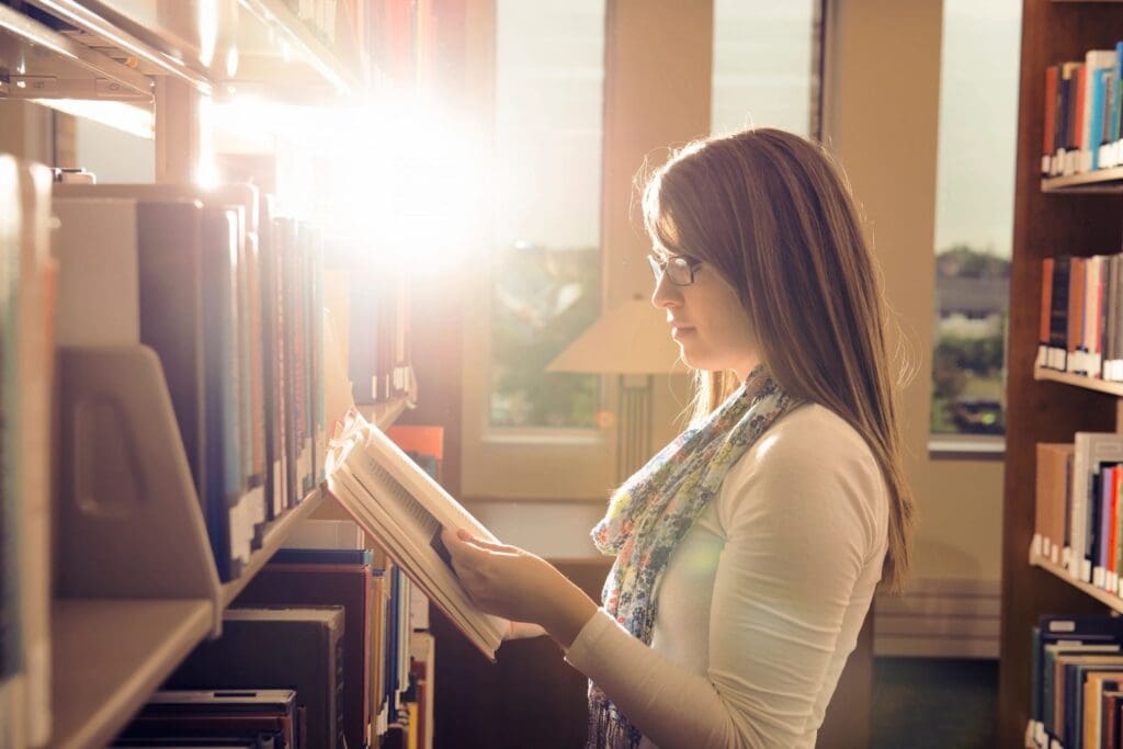 A woman is reading a book in a library.