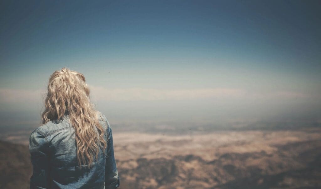 A woman with long blonde hair standing on top of a mountain.
