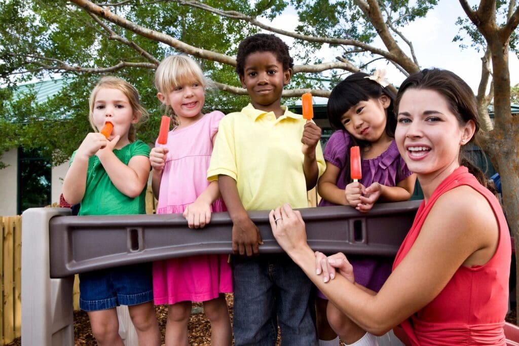 A woman holding carrots with children on a playground.