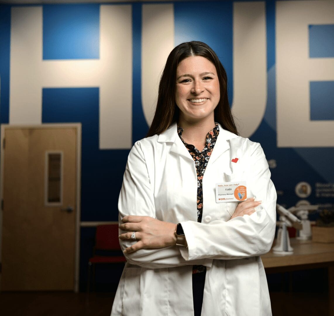 A woman in a lab coat standing in front of a blue wall.