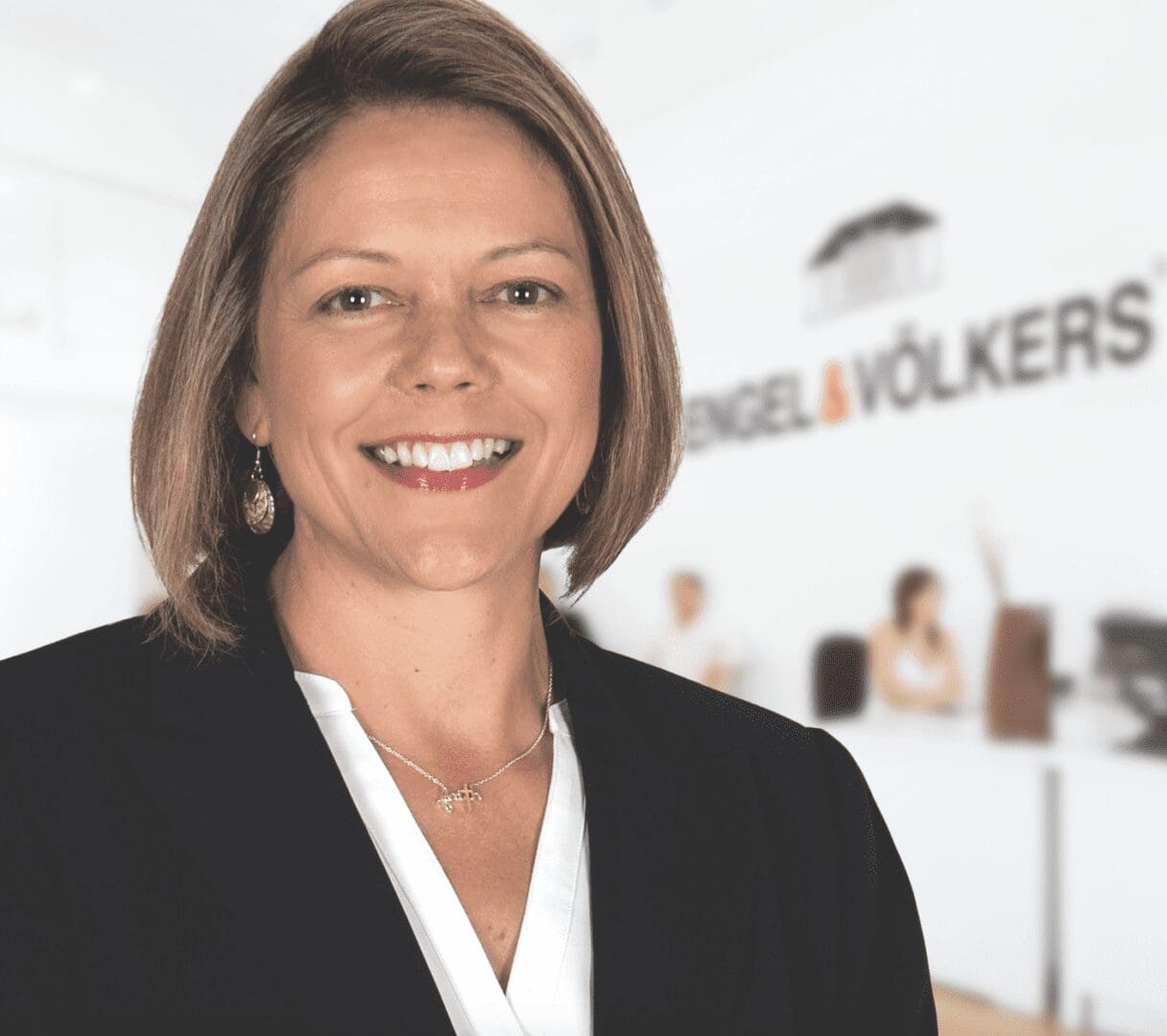 A woman in a business suit standing in front of a white wall.