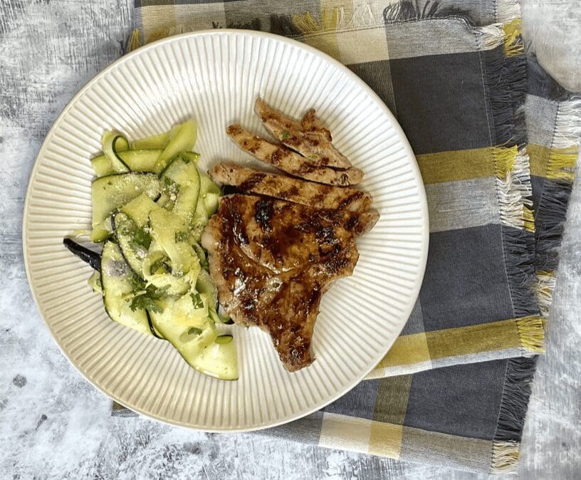 A plate with grilled pork chops and cucumbers.
