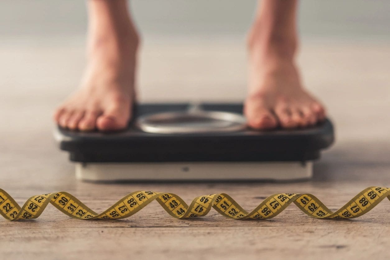 A person standing on a weight scale with a yellow tape.