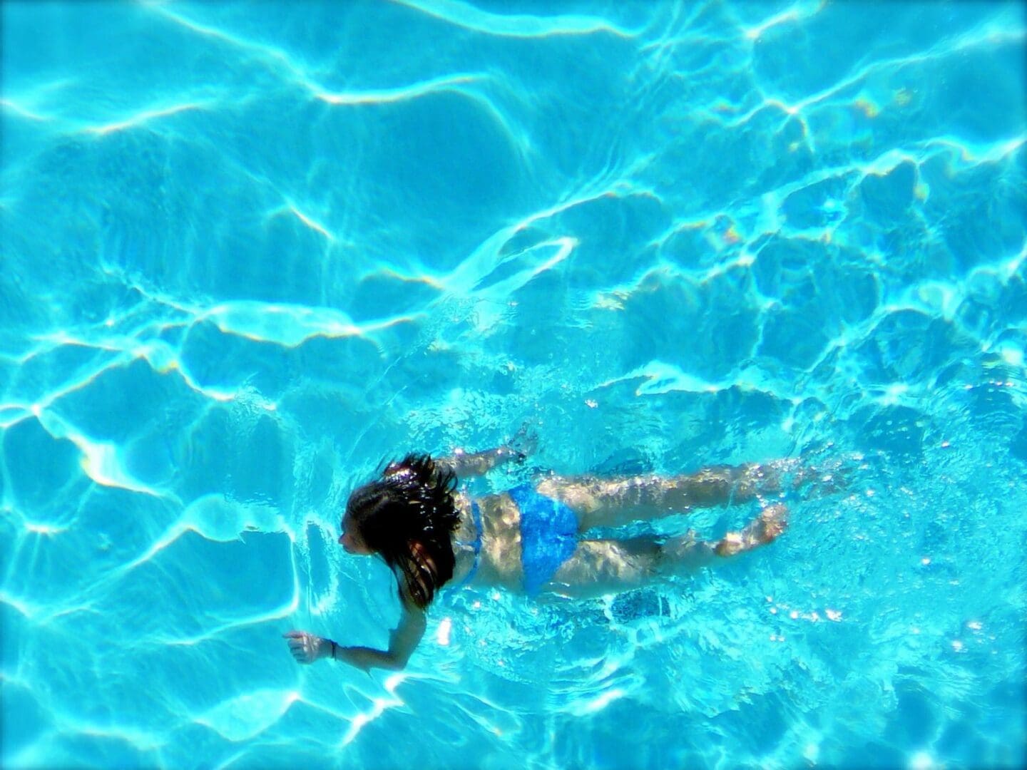 A woman in a blue bikini swimming in a blue pool.