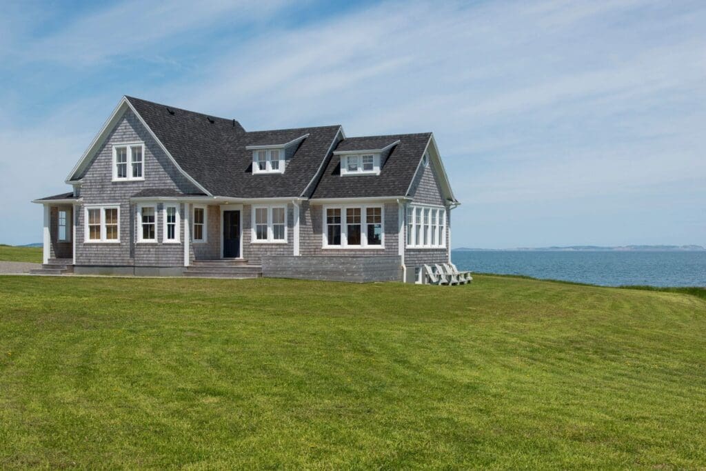 A gray house sits on a grassy hill overlooking the ocean.