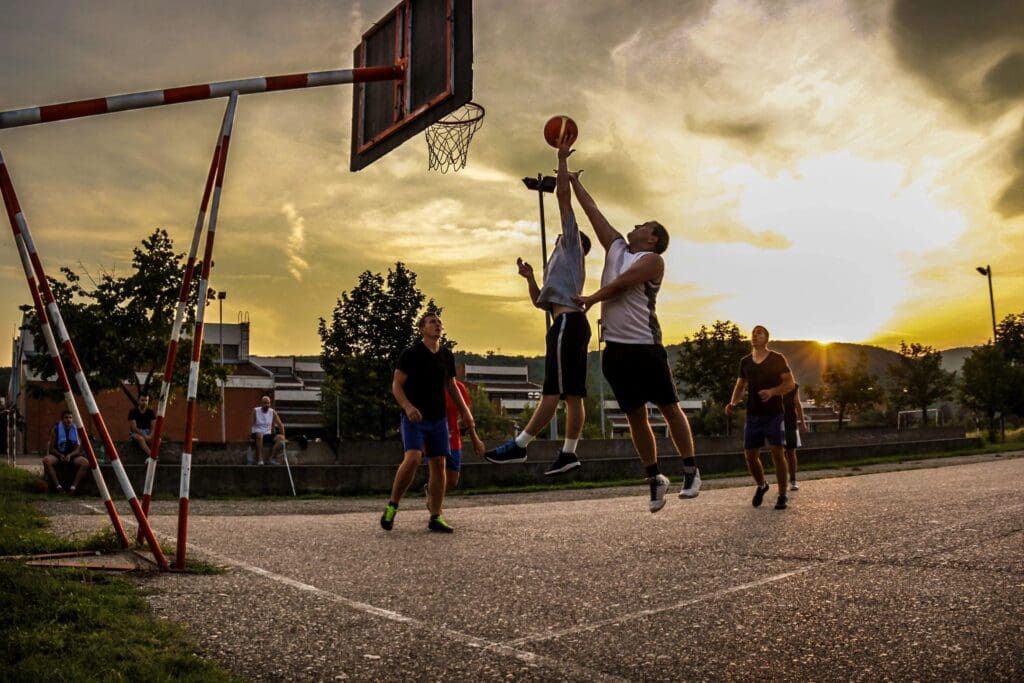 A group of people playing basketball at sunset.