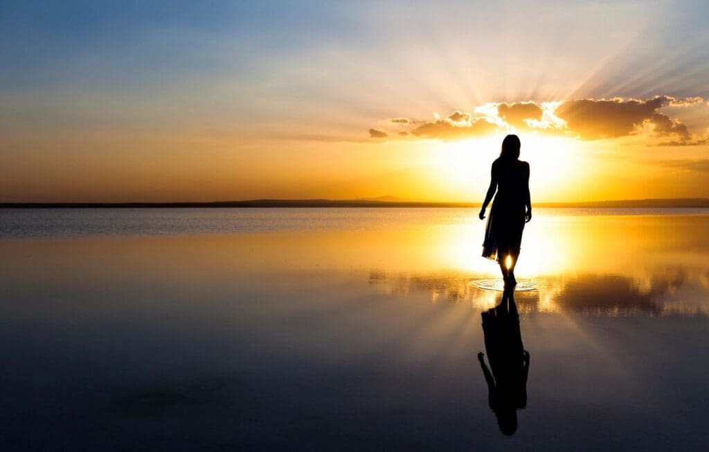 A silhouette of a woman walking in the water at sunset.