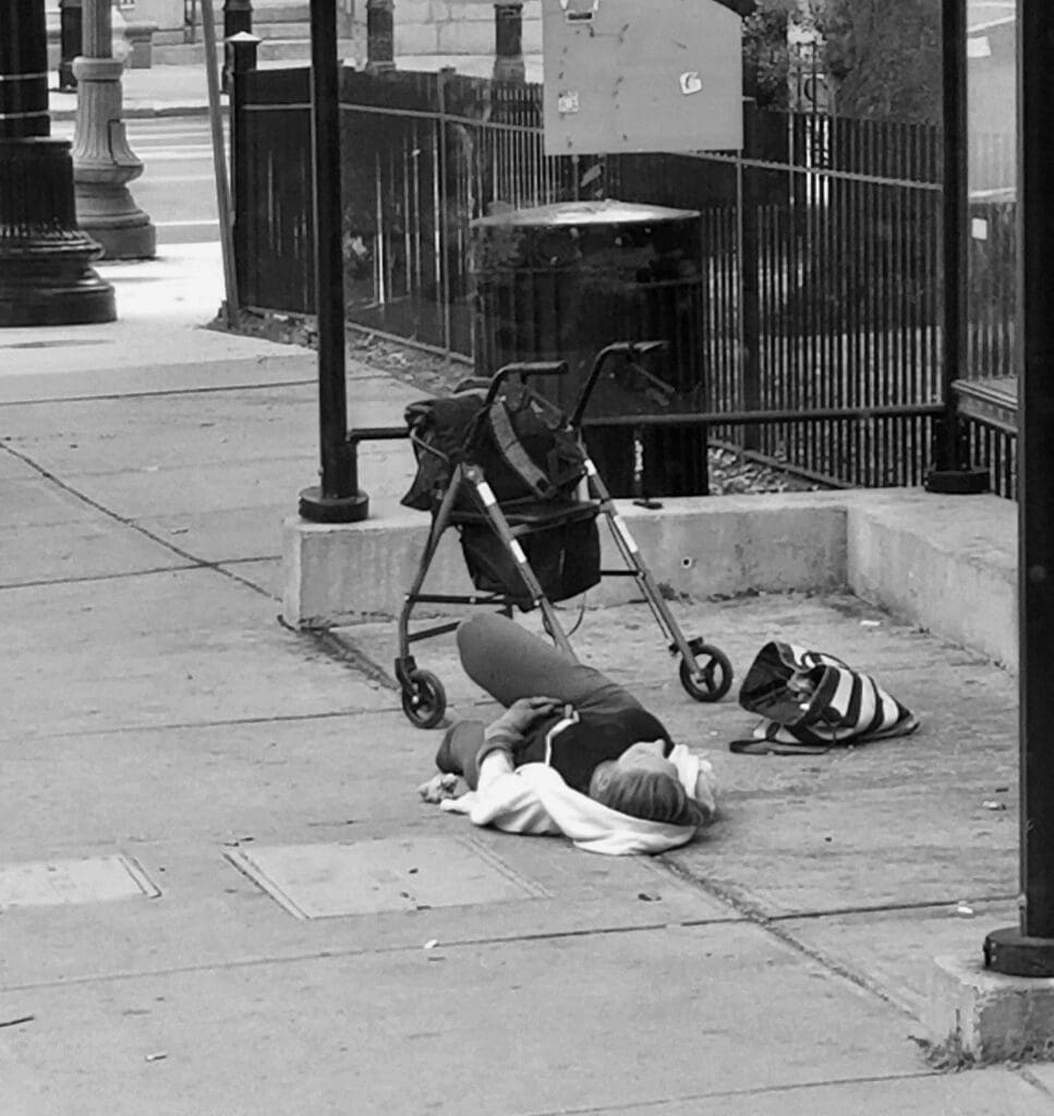 A person is laying on the sidewalk with a stroller.
