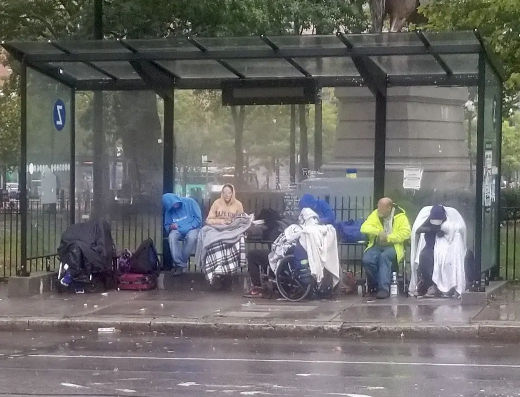 A group of people sitting at a bus stop in the rain.