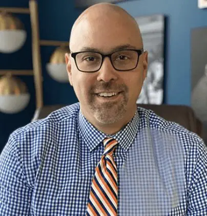 A bald man wearing glasses and a blue and orange tie.