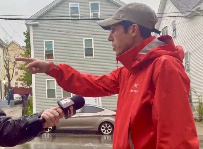 A man in a red jacket is talking to a reporter in a raincoat.