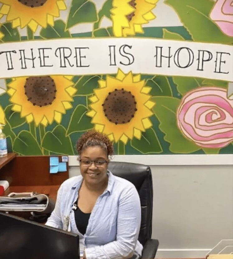 A woman sitting in front of a desk with sunflowers on the wall.