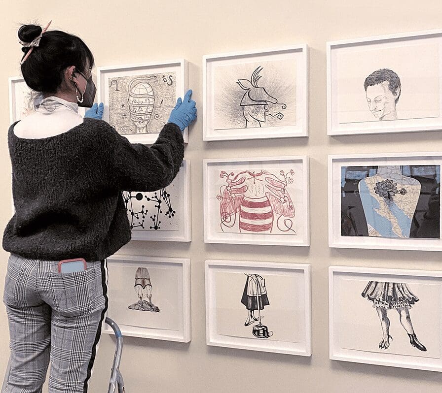 A woman looking at framed drawings on a wall.