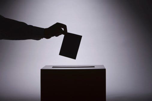 A person putting a voting card into a voting box.