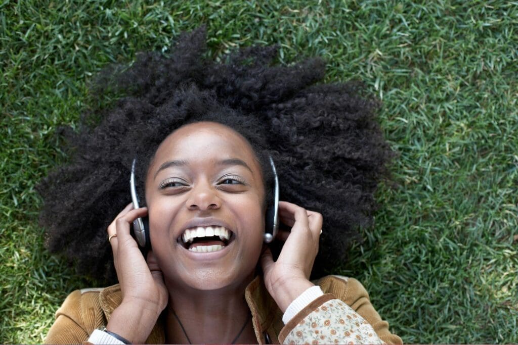 A young woman with afro hair listening to music in the grass.