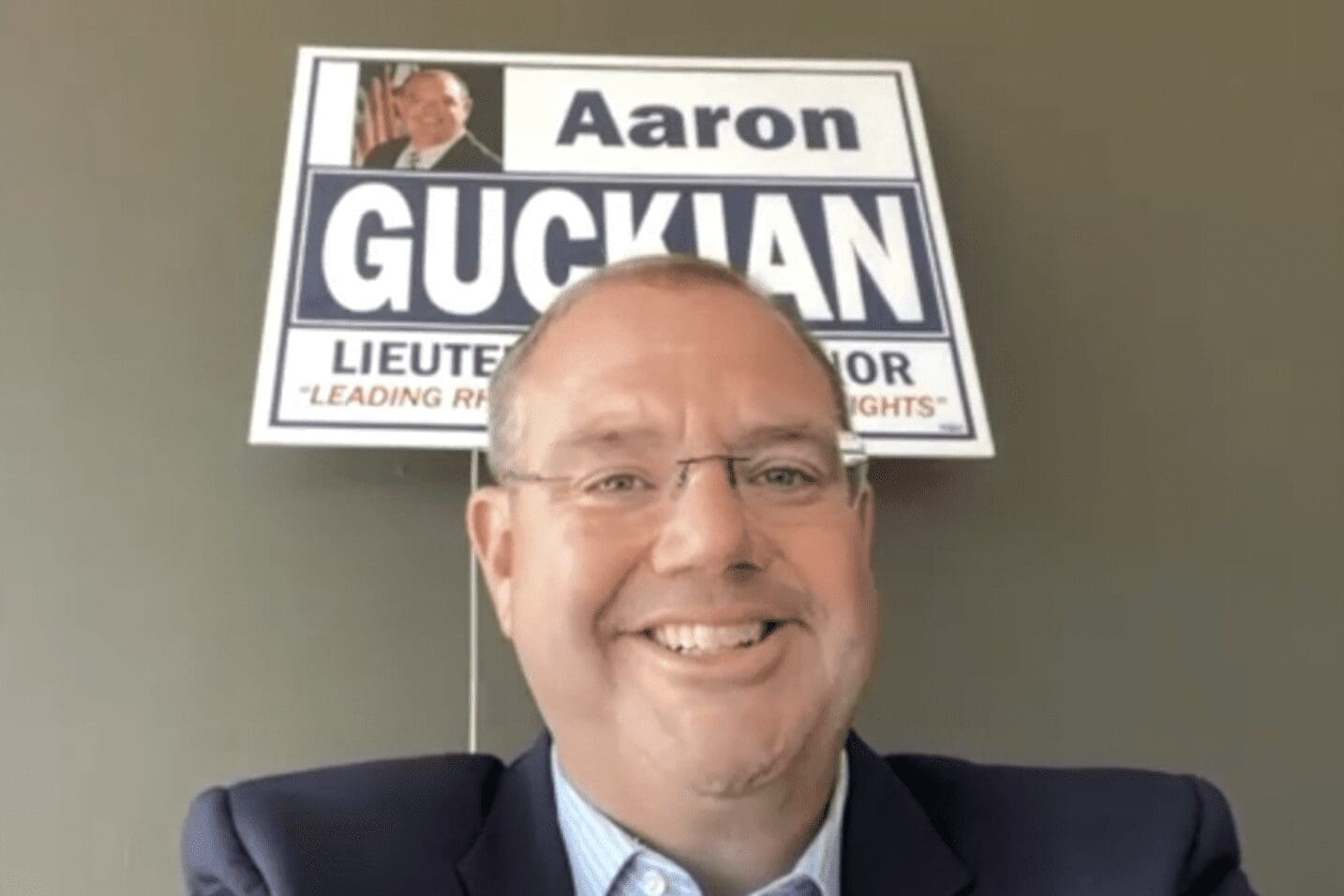 A man in a suit and tie is standing in front of a sign that says aaron guccian.