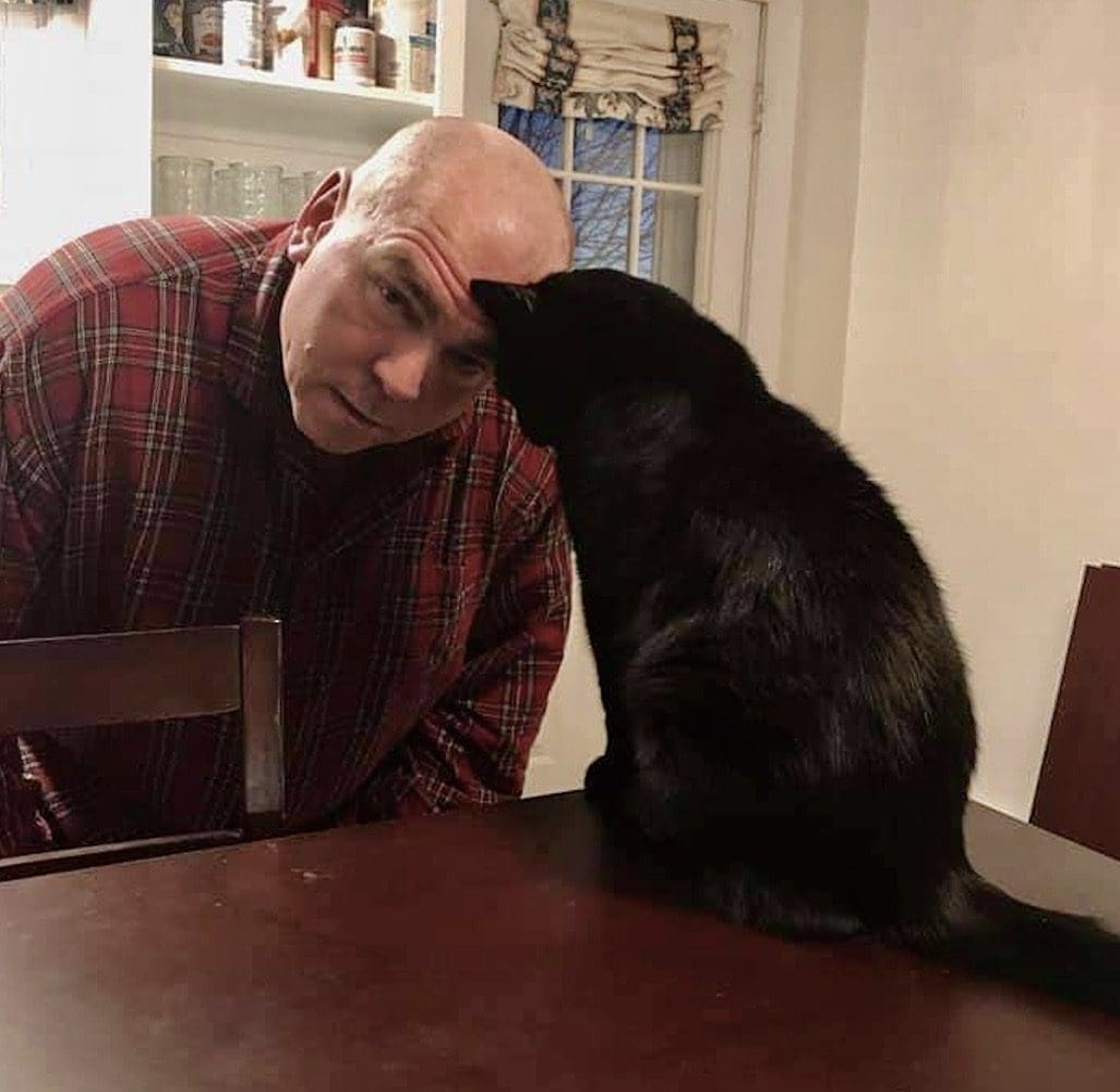 A man petting a black cat at a table.