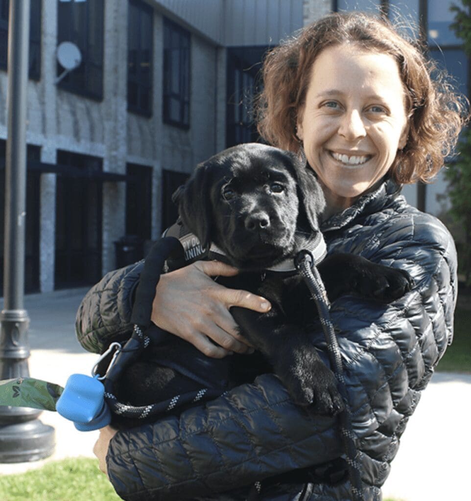 A woman holding a black labrador puppy.