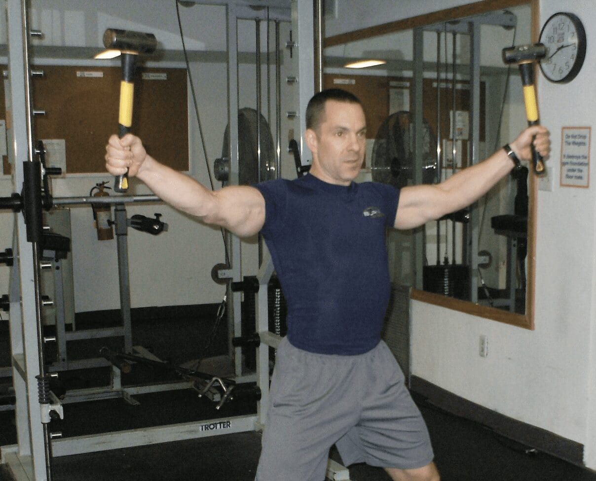 A man in a gym holding a pair of dumbbells.