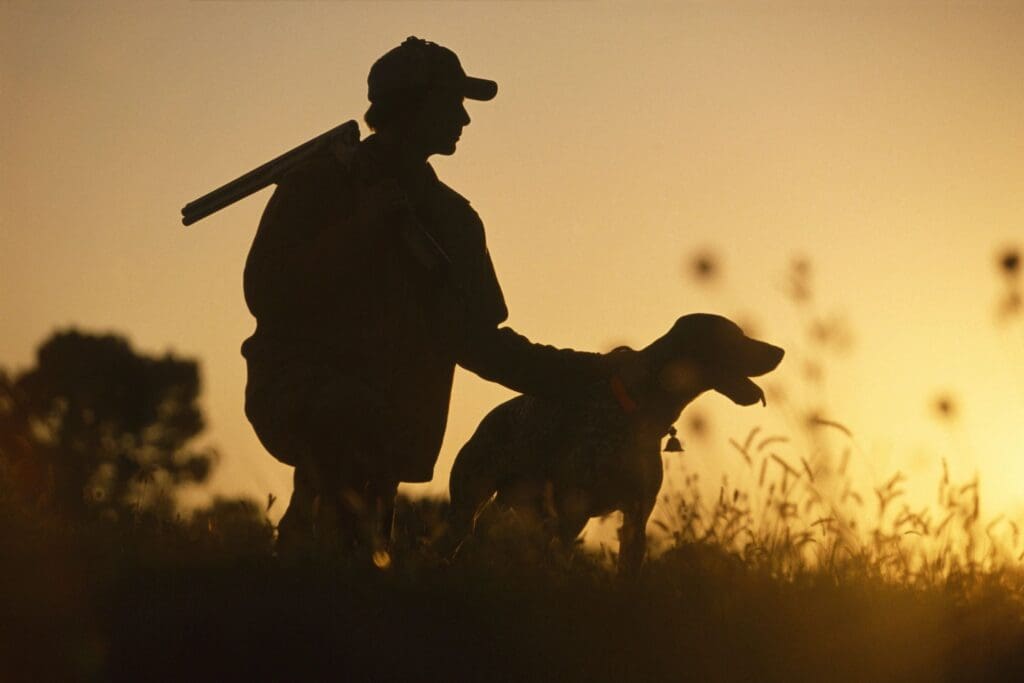 A silhouette of a man with a gun and a dog.