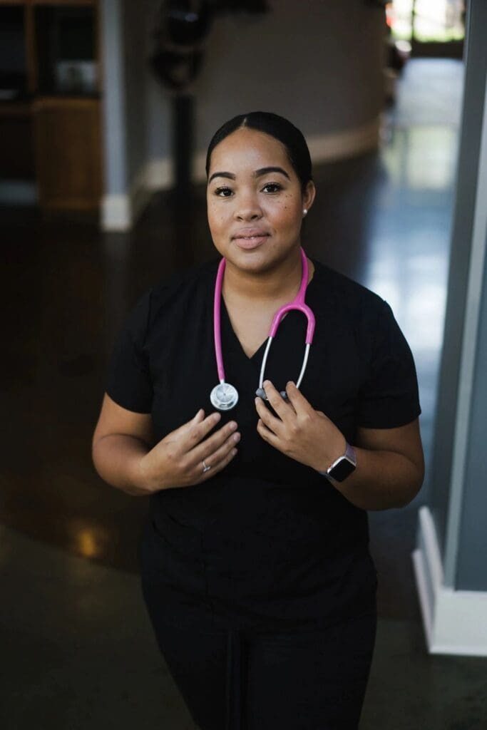 A woman wearing a black uniform with a pink stethoscope.