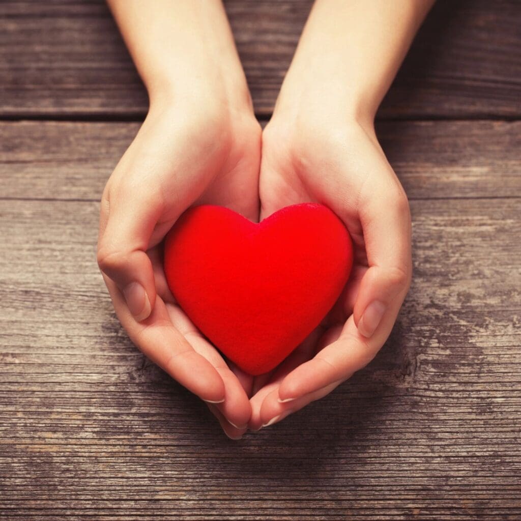 A woman's hands holding a red heart on a wooden table.