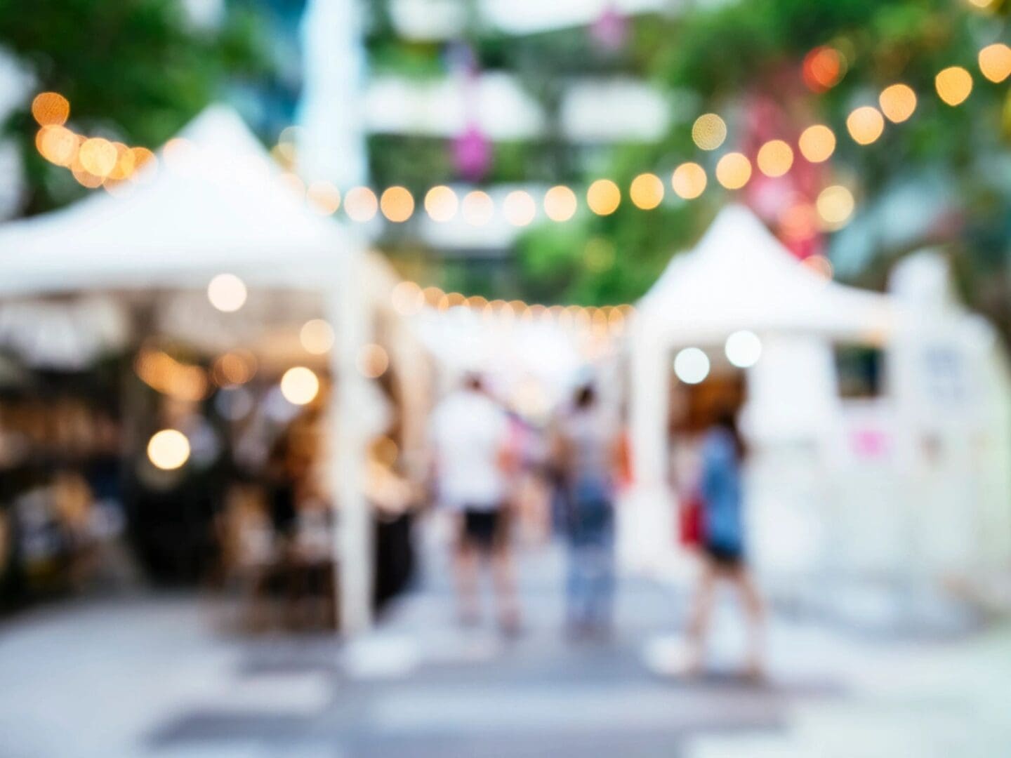 A blurry image of people walking in an outdoor market.