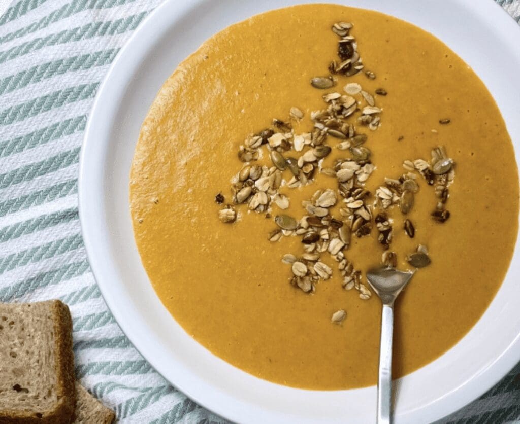 A bowl of pumpkin soup with granola and bread.