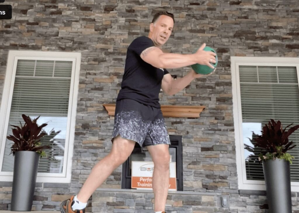 A man is doing a squat with a green ball.